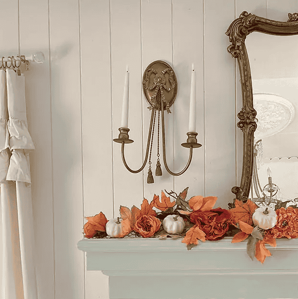 A charming fireplace mantle showcasing fall decor, complemented by a mirror and a brass wall candelabra for a warm ambiance.