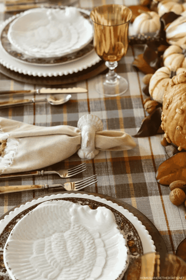 A charming table setting showcasing white plates, polished silverware, and vibrant pumpkins, perfect for a festive gathering.